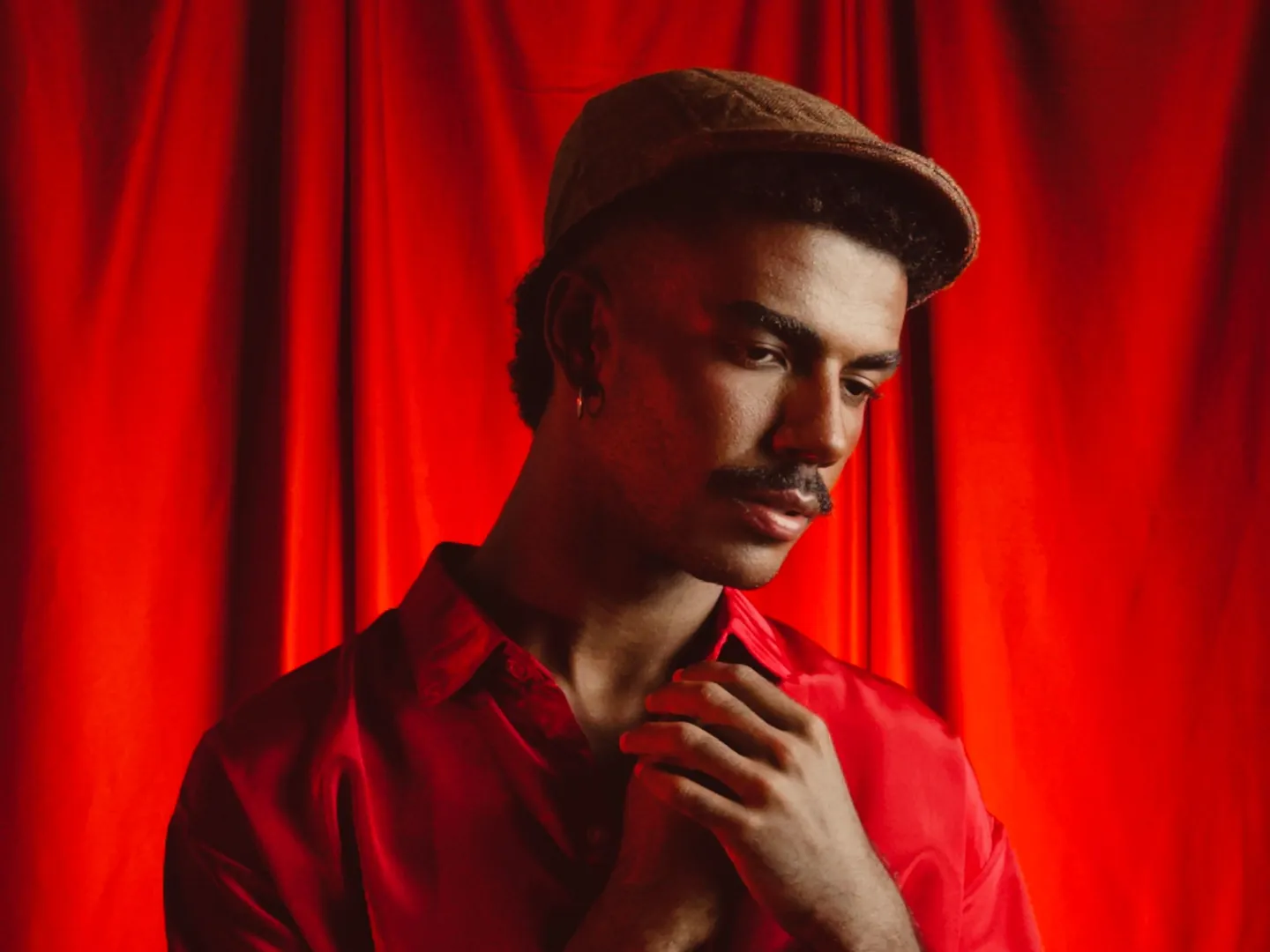 Un comédien en chemise rouge, pensif, devant un rideau de scène rouge