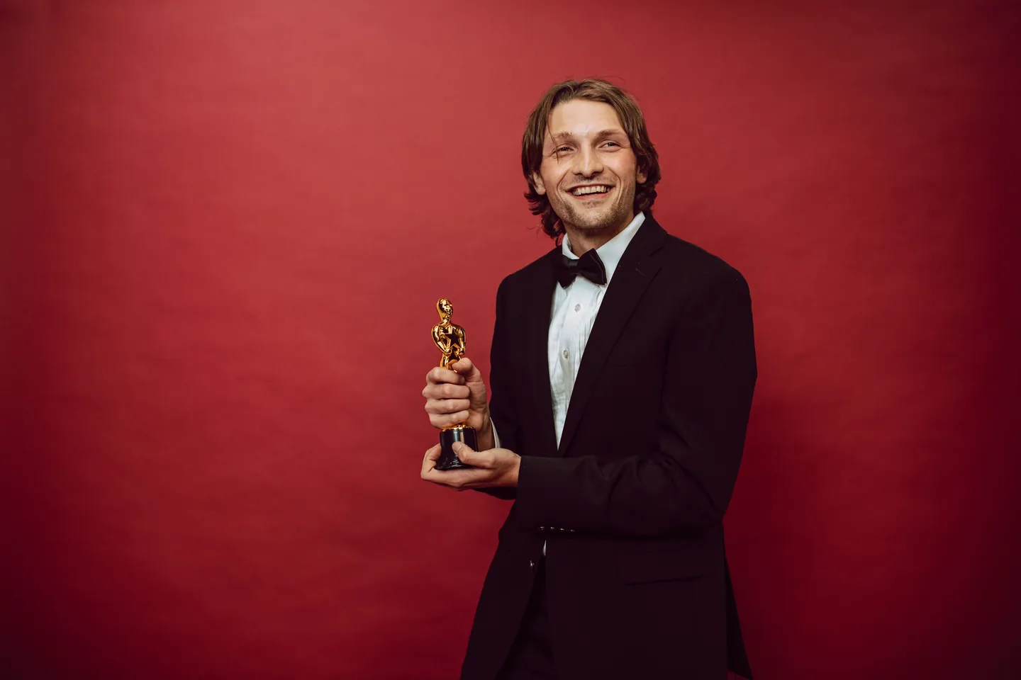 Un acteur en smoking, trophée à la main, sur fond rouge